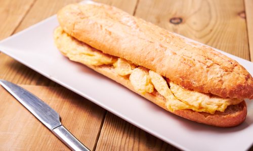 Close-up of tasty sandwich made of crispy baguette and omelette on wooden background.